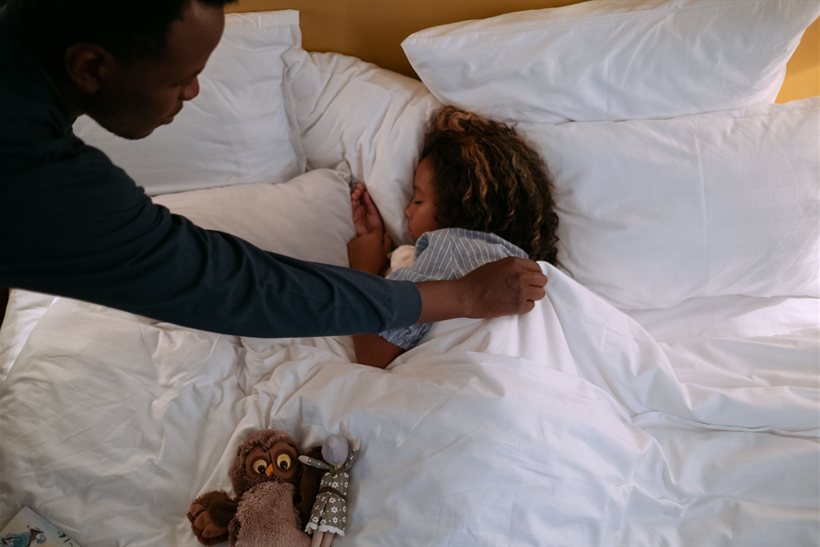 Father gently tucking his sleeping toddler into bed