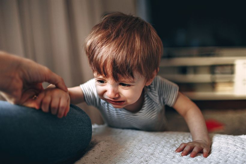 Upset toddler crying while a parent gently holds his hand at home